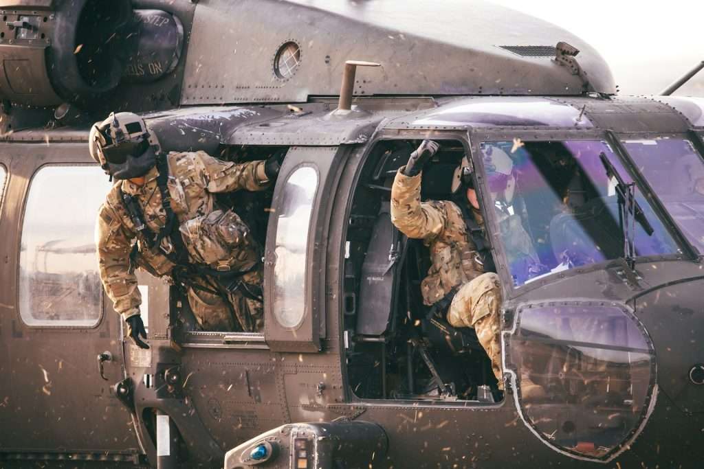 Military personnel in camouflage gear boarding or operating a helicopter.