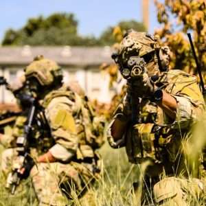 Team of soldiers in camouflage gear aiming tactical rifles in tall grass.
