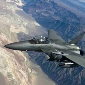 Fighter jet flying high above rugged mountains.
