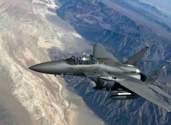 Fighter jet flying high above rugged mountains.