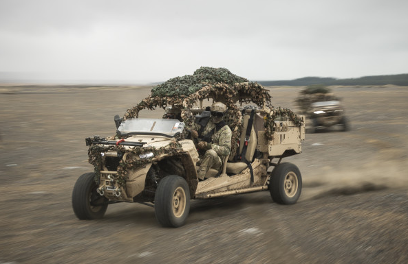 A military all-terrain vehicle driving across a field.
