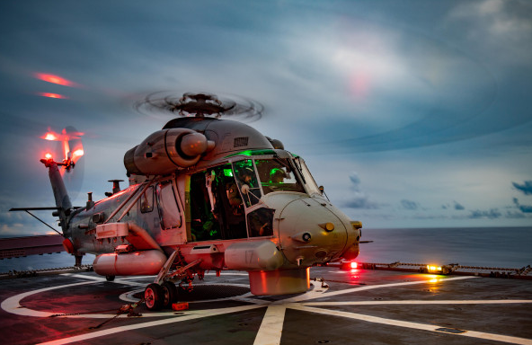 A military helicopter parked on a landing pad at dusk.