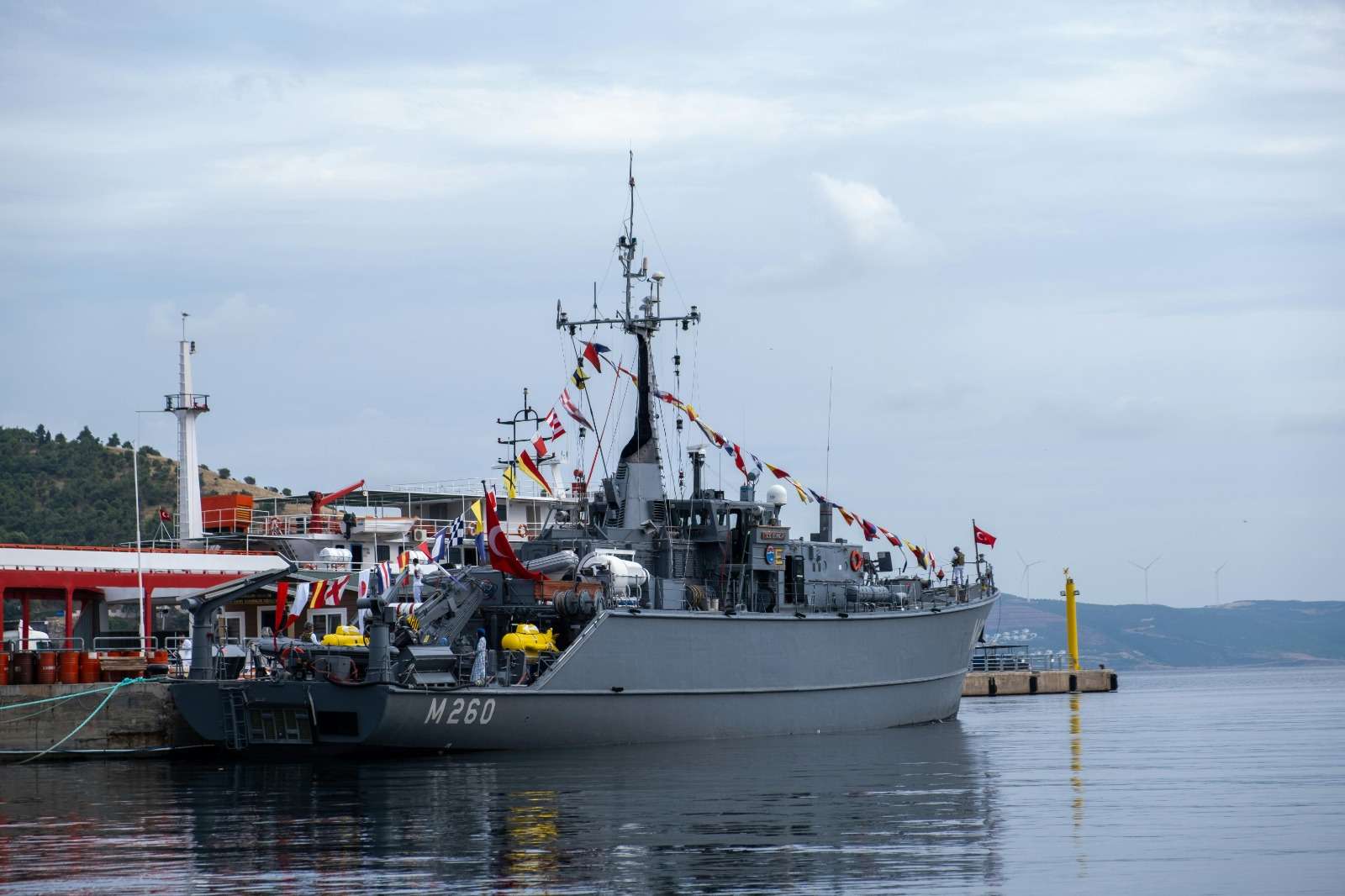 A military ship docked at a pier, decorated with colorful flags.
