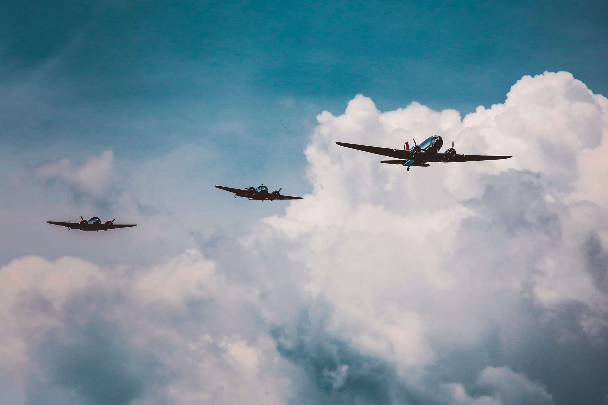 Three vintage airplanes flying in formation against a cloudy sky.