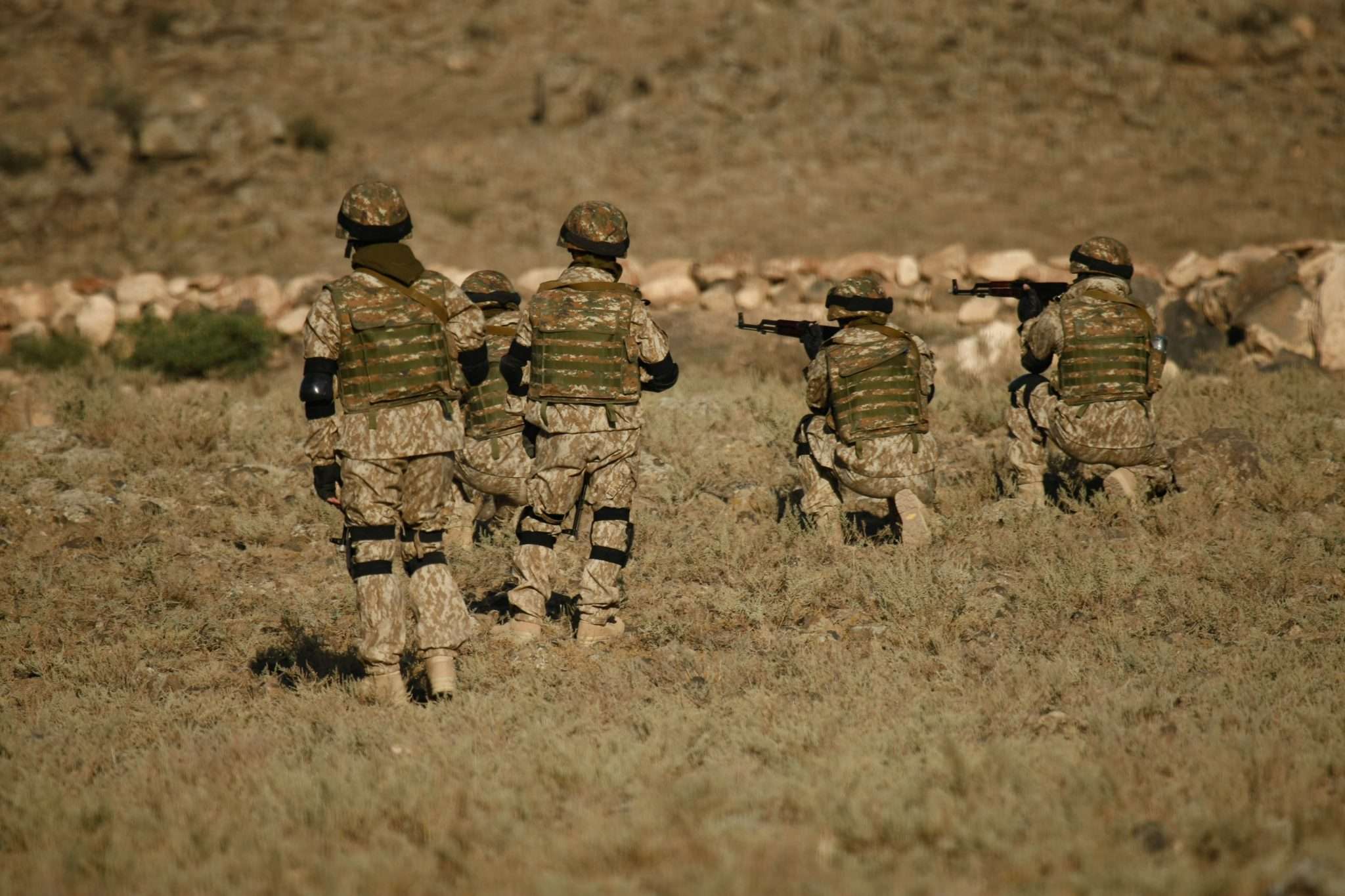 A group of soldiers in camouflage uniforms and helmets in a field.