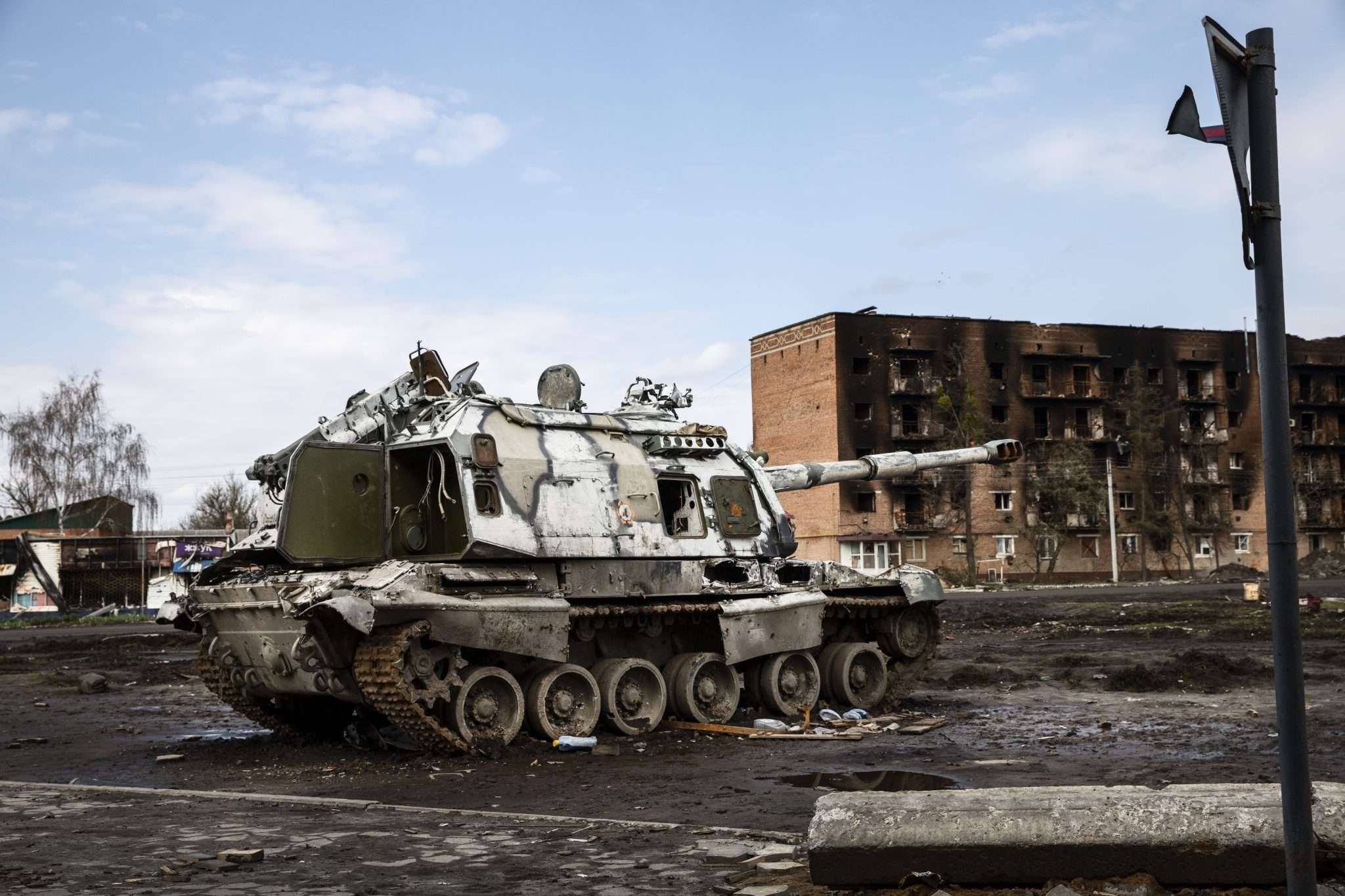 Destroyed military tank parked in a war-torn street near damaged buildings.