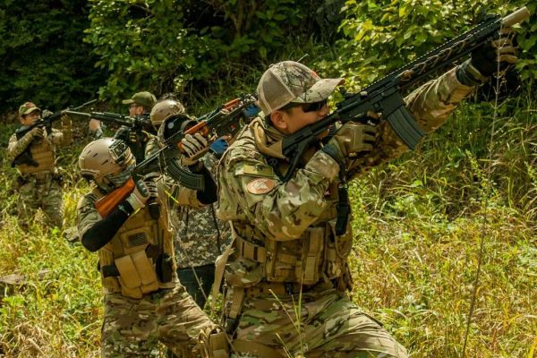 Team in tactical gear and camouflage holding rifles in a grassy field. Team in tactical gear and camouflage holding rifles in a grassy field.