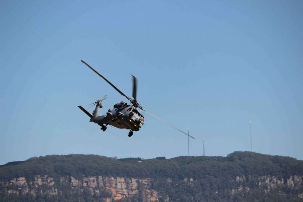 A military helicopter flying in the sky above a hilly landscape.