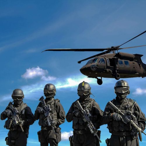Four tactical operators in black gear standing below a helicopter.